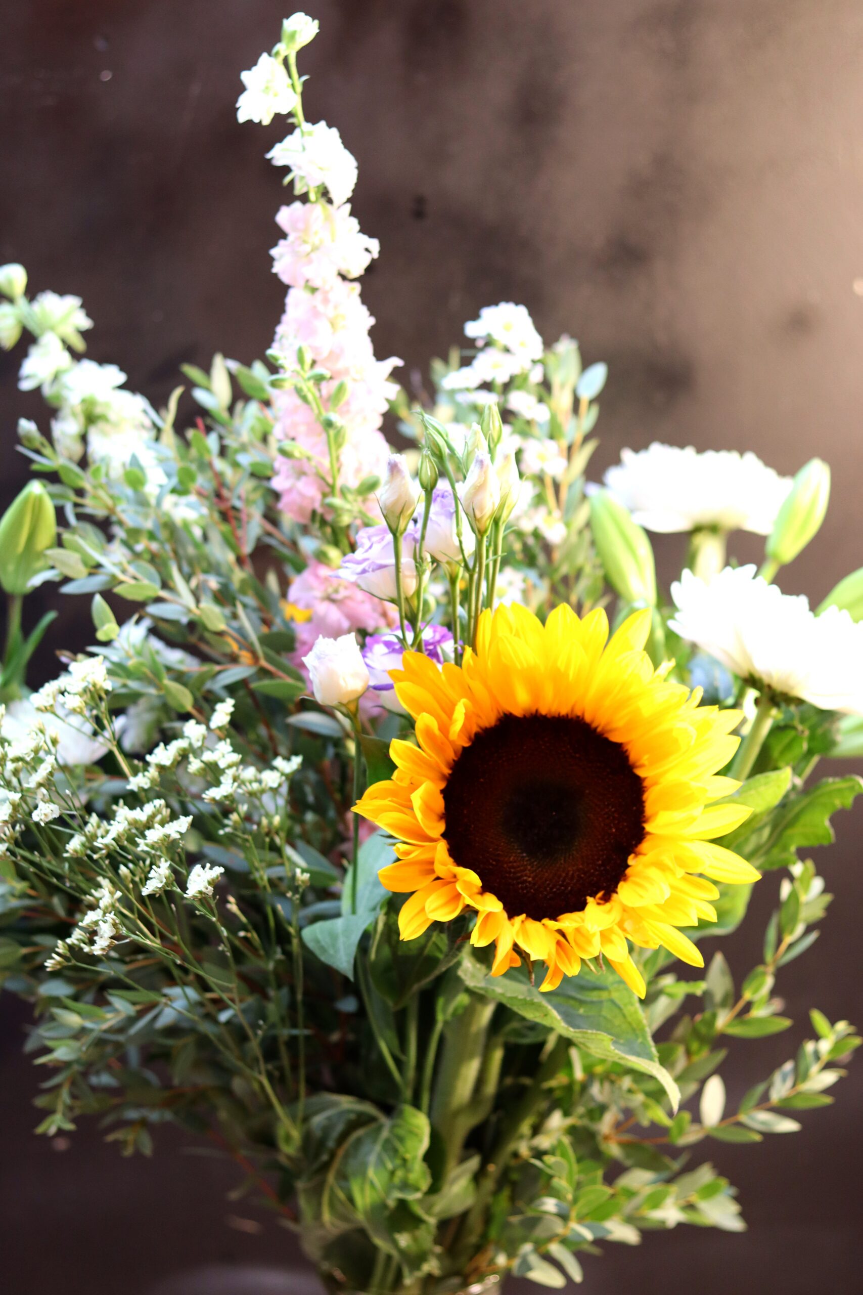 Scherpe close-up van een witte chrysant, met zonnebloem en groene lelieknoppen wazig op de achtergrond