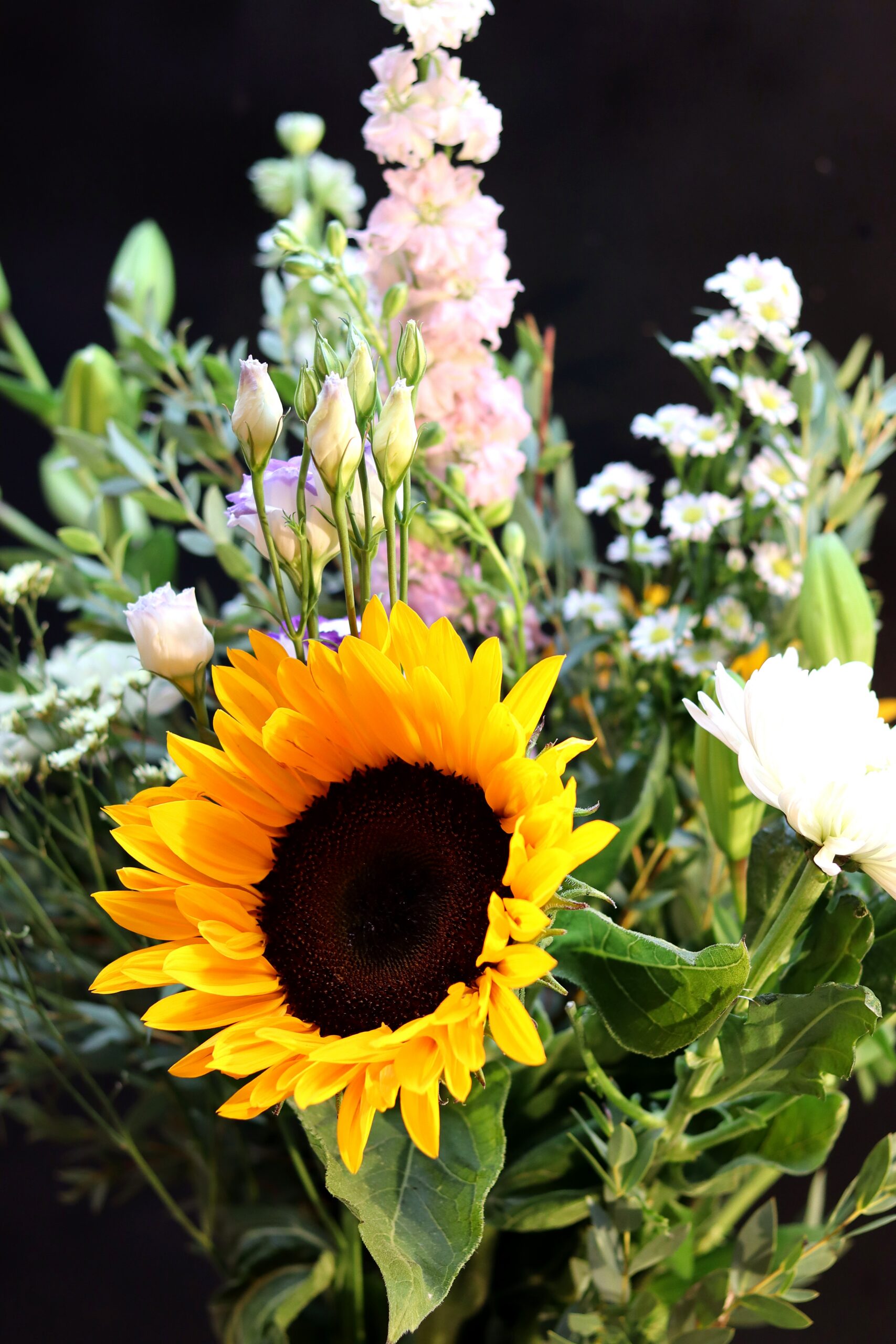 Close-up van het Zonnestraal Boeket met zonnebloem, witte chrysant, roze violieren en paarse lisianthusknoppen