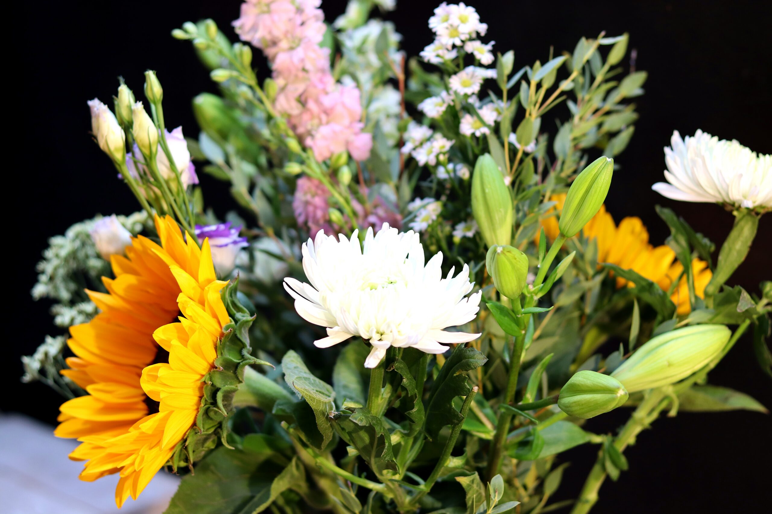 Scherpe close-up van een zonnebloem met wazige witte chrysant en paarse lisianthusknoppen op de achtergrond